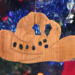 Handmade wooden Christmas tree ornament shaped like a cowboy hat, featuring a sprig of holly tucked into the hat band, star-shaped leaf cutouts, and round berry accents.