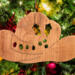 Handmade wooden Christmas tree ornament shaped like a cowboy hat, featuring a sprig of holly tucked into the hat band, star-shaped leaf cutouts, and round berry accents.