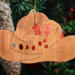Handmade wooden Christmas tree ornament shaped like a cowboy hat, featuring a sprig of holly tucked into the hat band, star-shaped leaf cutouts, and round berry accents.