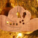 Handmade wooden Christmas tree ornament shaped like a cowboy hat, featuring a sprig of holly tucked into the hat band, star-shaped leaf cutouts, and round berry accents.