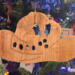 Handmade wooden Christmas tree ornament shaped like a cowboy hat, featuring a sprig of holly tucked into the hat band, star-shaped leaf cutouts, and round berry accents.