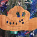 Handmade wooden Christmas tree ornament shaped like a cowboy hat, featuring a sprig of holly tucked into the hat band, star-shaped leaf cutouts, and round berry accents.
