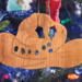 Handmade wooden Christmas tree ornament shaped like a cowboy hat, featuring a sprig of holly tucked into the hat band, star-shaped leaf cutouts, and round berry accents.