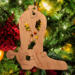 Handmade wooden Christmas tree ornament shaped like a cowboy boot, featuring a sprig of holly On the side of the boot, and round berry accents.