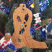 Handmade wooden Christmas tree ornament shaped like a cowboy boot, featuring a sprig of holly On the side of the boot, and round berry accents.