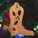 Handmade wooden Christmas tree ornament shaped like a cowboy boot, featuring a sprig of holly On the side of the boot, and round berry accents.