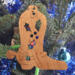 Handmade wooden Christmas tree ornament shaped like a cowboy boot, featuring a sprig of holly On the side of the boot, and round berry accents.