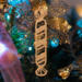 Handmade wooden Christmas tree ornament shaped like a peppermint stick with diagonal stripes, crafted from light-colored wood with flared decorative ends.
