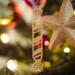 Handmade wooden Christmas tree ornament shaped like a peppermint stick with diagonal stripes, crafted from light-colored wood with flared decorative ends.