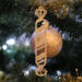 Handmade wooden Christmas tree ornament shaped like a peppermint stick with diagonal stripes, crafted from light-colored wood with flared decorative ends.