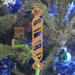 Handmade wooden Christmas tree ornament shaped like a peppermint stick with diagonal stripes, crafted from light-colored wood with flared decorative ends.