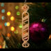 Handmade wooden Christmas tree ornament shaped like a peppermint stick with diagonal stripes, crafted from light-colored wood with flared decorative ends.