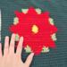 A close up of one of the red poinsettias on either end of the table runner. The maker's hand is in the photo to the left to show size.  A close up of one of the red poinsettias on either end of the table runner. The maker's hand is in the photo to the left to show size.
