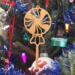 A handcrafted wooden Christmas tree ornament shaped like a lollipop, featuring intricate cut-out spiral patterns on the circular top and a simple stick base. The ornament is light brown with a smooth finish.