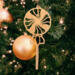 A handcrafted wooden Christmas tree ornament shaped like a lollipop, featuring intricate cut-out spiral patterns on the circular top and a simple stick base. The ornament is light brown with a smooth finish.