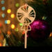 A handcrafted wooden Christmas tree ornament shaped like a lollipop, featuring intricate cut-out spiral patterns on the circular top and a simple stick base. The ornament is light brown with a smooth finish.