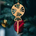A handcrafted wooden Christmas tree ornament shaped like a lollipop, featuring intricate cut-out spiral patterns on the circular top and a simple stick base. The ornament is light brown with a smooth finish.