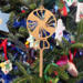 A handcrafted wooden Christmas tree ornament shaped like a lollipop, featuring intricate cut-out spiral patterns on the circular top and a simple stick base. The ornament is light brown with a smooth finish.