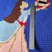 A close up of the ballerina's dress on the blanket. She has brown hair, a blue jacket, and pink dress with red ribbon belt. 
