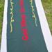 A dark green and red table runner with God Bless Us Every One in the center, poinsettias on either end. And yellow swirls around the quote. A dark green and red table runner with God Bless Us Every One in the center, poinsettias on either end. And yellow swirls around the quote.
