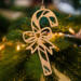 Handmade wooden Christmas tree ornament shaped like a curved candy cane with intricate stripe cutouts, accented by a delicate bow and crafted from natural light colored wood tones.