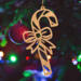 Handmade wooden Christmas tree ornament shaped like a curved candy cane with intricate stripe cutouts, accented by a delicate bow and crafted from natural light colored wood tones.