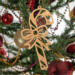 Handmade wooden Christmas tree ornament shaped like a curved candy cane with intricate stripe cutouts, accented by a delicate bow and crafted from natural light colored wood tones.
