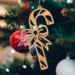 Handmade wooden Christmas tree ornament shaped like a curved candy cane with intricate stripe cutouts, accented by a delicate bow and crafted from natural light colored wood tones.