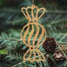 A handmade wooden Christmas tree ornament shaped like a wrapped hard candy, featuring a bulbous center with swirling stripes and twisted wrapper ends, crafted from light-toned wood using a scroll saw.