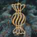 A handmade wooden Christmas tree ornament shaped like a wrapped hard candy, featuring a bulbous center with swirling stripes and twisted wrapper ends, crafted from light-toned wood using a scroll saw.