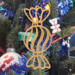 A handmade wooden Christmas tree ornament shaped like a wrapped hard candy, featuring a bulbous center with swirling stripes and twisted wrapper ends, crafted from light-toned wood using a scroll saw.