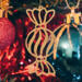 A handmade wooden Christmas tree ornament shaped like a wrapped hard candy, featuring a bulbous center with swirling stripes and twisted wrapper ends, crafted from light-toned wood using a scroll saw.