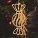 A handmade wooden Christmas tree ornament shaped like a wrapped hard candy, featuring a bulbous center with swirling stripes and twisted wrapper ends, crafted from light-toned wood using a scroll saw.