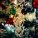 A handcrafted wooden Christmas tree ornament shaped like a wrapped candy, featuring intricate Victorian fretwork with twisted ends and a diagonal swirling stripe in the center.