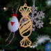 A handcrafted wooden Christmas tree ornament shaped like a wrapped candy, featuring intricate Victorian fretwork with twisted ends and a diagonal swirling stripe in the center.