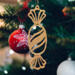 A handcrafted wooden Christmas tree ornament shaped like a wrapped candy, featuring intricate Victorian fretwork with twisted ends and a diagonal swirling stripe in the center.