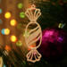 A handcrafted wooden Christmas tree ornament shaped like a wrapped candy, featuring intricate Victorian fretwork with twisted ends and a diagonal swirling stripe in the center.