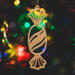 A handcrafted wooden Christmas tree ornament shaped like a wrapped candy, featuring intricate Victorian fretwork with twisted ends and a diagonal swirling stripe in the center.