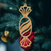 A handcrafted wooden Christmas tree ornament shaped like a wrapped candy, featuring intricate Victorian fretwork with twisted ends and a diagonal swirling stripe in the center.