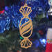 A handcrafted wooden Christmas tree ornament shaped like a wrapped candy, featuring intricate Victorian fretwork with twisted ends and a diagonal swirling stripe in the center.