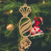 A handcrafted wooden Christmas tree ornament shaped like a wrapped candy, featuring intricate Victorian fretwork with twisted ends and a diagonal swirling stripe in the center.