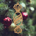 A handcrafted wooden Christmas tree ornament shaped like a wrapped candy, featuring intricate Victorian fretwork with twisted ends and a diagonal swirling stripe in the center.