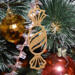 A handcrafted wooden Christmas tree ornament shaped like a wrapped candy, featuring intricate Victorian fretwork with twisted ends and a diagonal swirling stripe in the center.