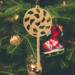 A handmade Christmas tree ornament crafted from light brown maple hardwood plywood, shaped like a lollipop with a round head featuring intricate spiral cutouts and a long stick handle, suspended from a small metal hook.