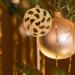 A handmade Christmas tree ornament crafted from light brown maple hardwood plywood, shaped like a lollipop with a round head featuring intricate spiral cutouts and a long stick handle, suspended from a small metal hook.