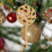 A handmade Christmas tree ornament crafted from light brown maple hardwood plywood, shaped like a lollipop with a round head featuring intricate spiral cutouts and a long stick handle, suspended from a small metal hook.