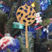 A handmade Christmas tree ornament crafted from light brown maple hardwood plywood, shaped like a lollipop with a round head featuring intricate spiral cutouts and a long stick handle, suspended from a small metal hook.