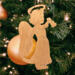 A handmade wooden Christmas ornament in the shape of a cheerful angel, featuring a halo, wings, and a raised arm ringing a bell, hand-cut from solid hardwood and finished with clear shellac.