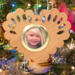 Wooden heart-shaped ornament with scalloped edges and an oak grain finish, featuring a removable round gold frame that holds a photo of a smiling blonde child.
