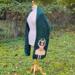 A side shot of the scarf hanging from the white dress form. Tehre is green grass in the background. A side shot of the scarf hanging from the white dress form. Tehre is green grass in the background.